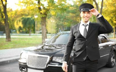 Young chauffeur adjusting hat near luxury car on the street